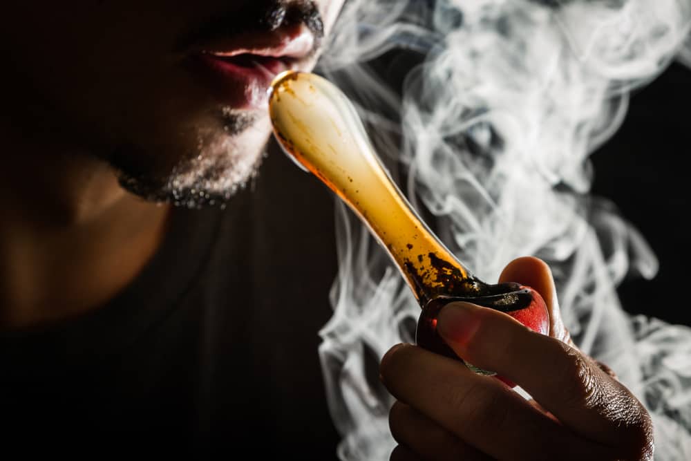 Person smoking marijuana from a blown glass pipe.