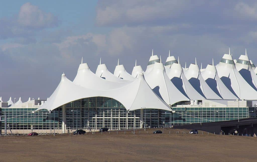 The exterior view of Denver International Airport with a white tent like roof with numerous peaks.